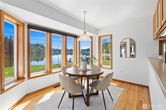 dining room with light wood-style floors, a water view, baseboards, and visible vents