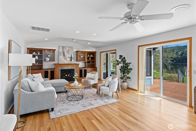 living room with lofted ceiling, wood finished floors, visible vents, baseboards, and ceiling fan