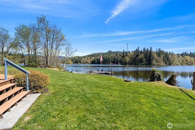 view of yard with a wooded view, a dock, and a water view