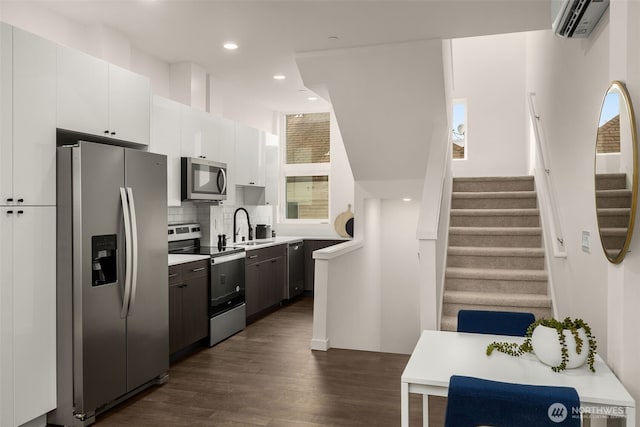 kitchen with dark wood-type flooring, white cabinetry, appliances with stainless steel finishes, a wall mounted AC, and backsplash
