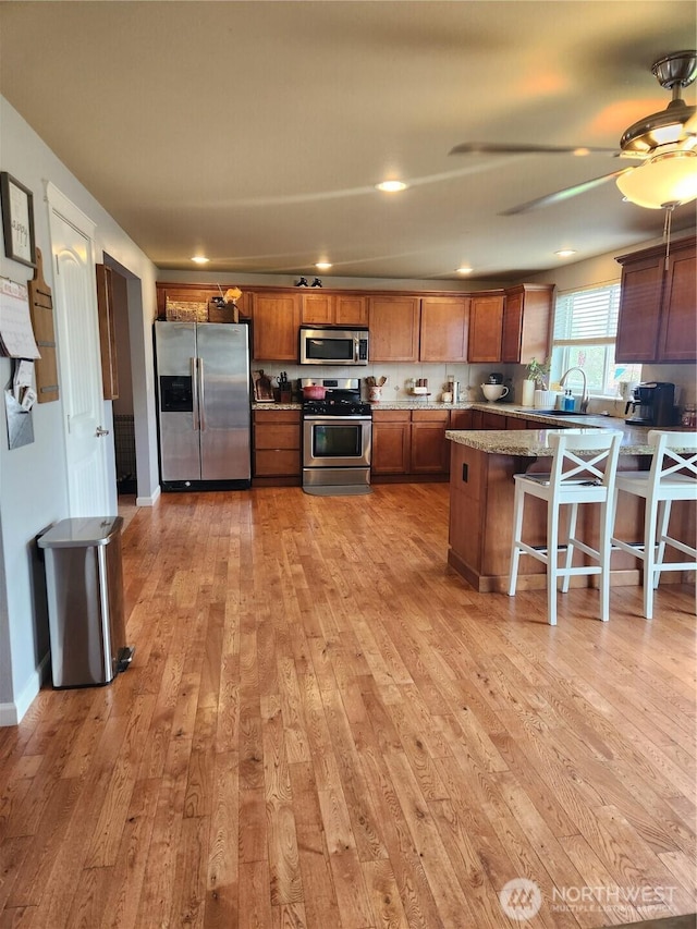 9244 Carys St SE, Yelm, WA 98597 - kitchen with light wood finished floors, stainless steel appliances, a kitchen bar, a ceiling fan, and brown cabinetry