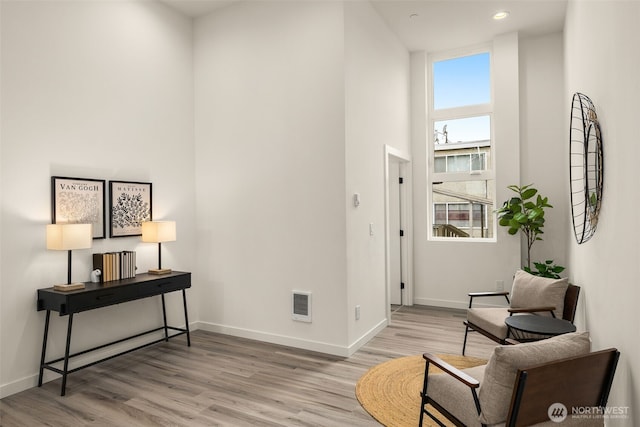 sitting room featuring visible vents, baseboards, a towering ceiling, and wood finished floors