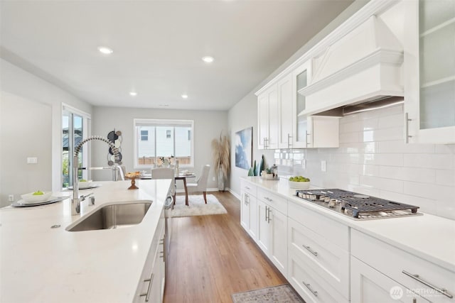 kitchen with stainless steel gas cooktop, custom exhaust hood, a sink, light countertops, and light wood finished floors