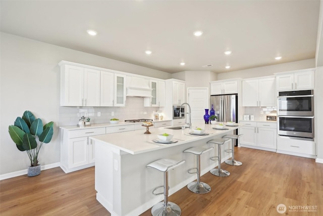 kitchen featuring a sink, stainless steel appliances, a kitchen bar, backsplash, and white cabinetry