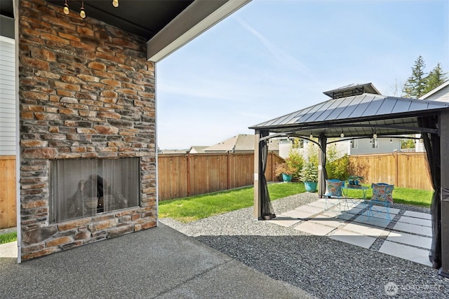 view of patio / terrace with a gazebo, a fenced backyard, and an outdoor brick fireplace