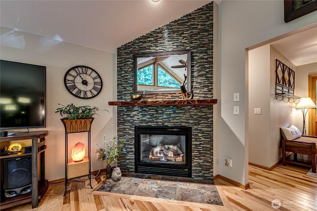 living area featuring baseboards, wood finished floors, vaulted ceiling, and a fireplace