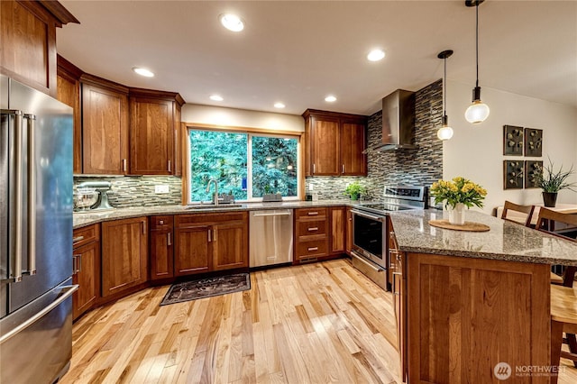 kitchen featuring tasteful backsplash, wall chimney range hood, appliances with stainless steel finishes, light wood finished floors, and a sink
