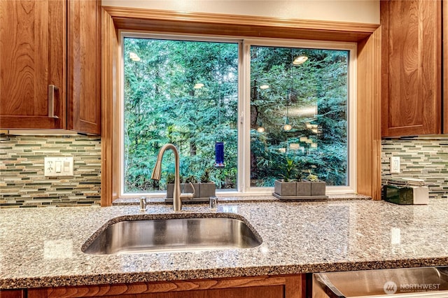 kitchen with brown cabinetry, a sink, light stone counters, and decorative backsplash