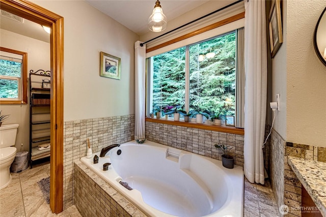 bathroom featuring a garden tub, visible vents, a wainscoted wall, toilet, and tile walls