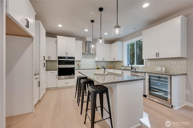 kitchen with light wood-type flooring, wine cooler, a sink, and wall chimney range hood