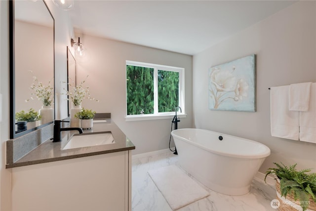 bathroom featuring a sink, marble finish floor, double vanity, a freestanding bath, and baseboards