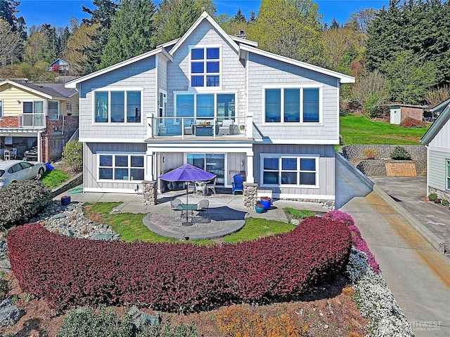 rear view of house with board and batten siding, a balcony, and a patio