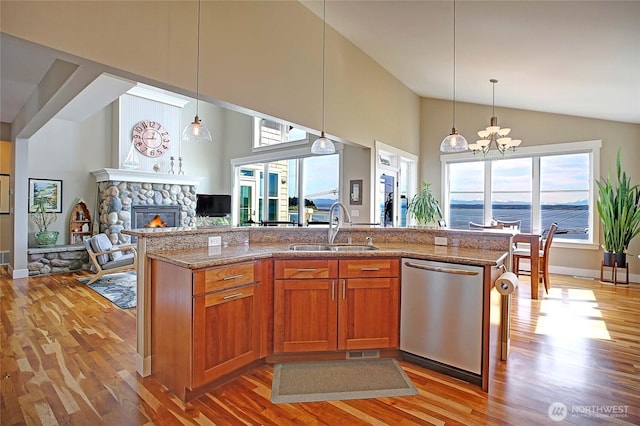 kitchen with brown cabinets, stainless steel dishwasher, a sink, light wood-type flooring, and open floor plan