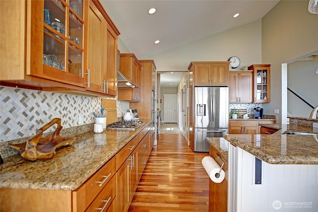 kitchen featuring stainless steel appliances, a sink, light wood-style floors, decorative backsplash, and brown cabinets
