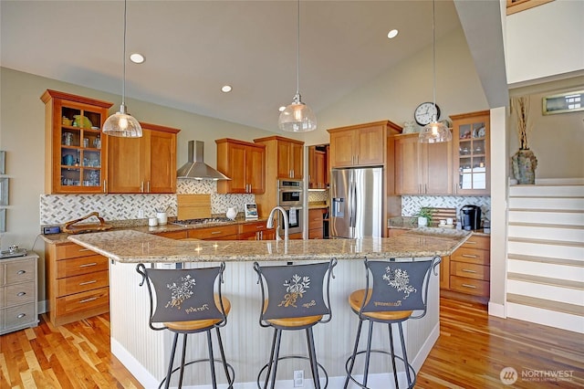 kitchen featuring wall chimney exhaust hood, stainless steel appliances, light wood-style flooring, and brown cabinets