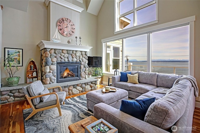living room with a stone fireplace, a high ceiling, and wood finished floors