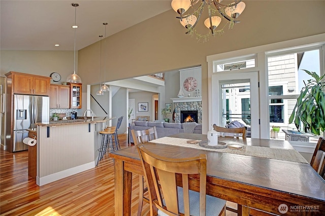 dining area with light wood finished floors, french doors, a fireplace, high vaulted ceiling, and a notable chandelier