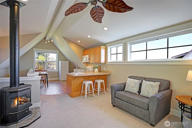 interior space with a peninsula, light carpet, a ceiling fan, white appliances, and a wood stove