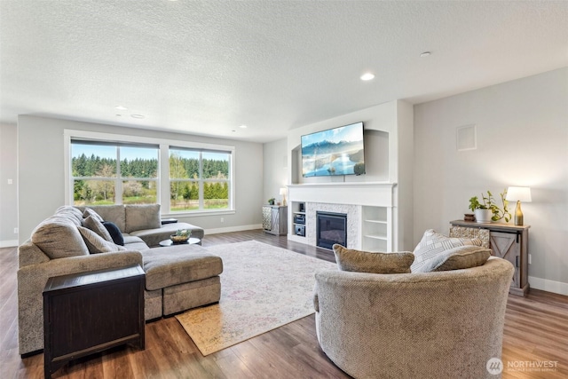 living area with baseboards, wood finished floors, a textured ceiling, and a fireplace