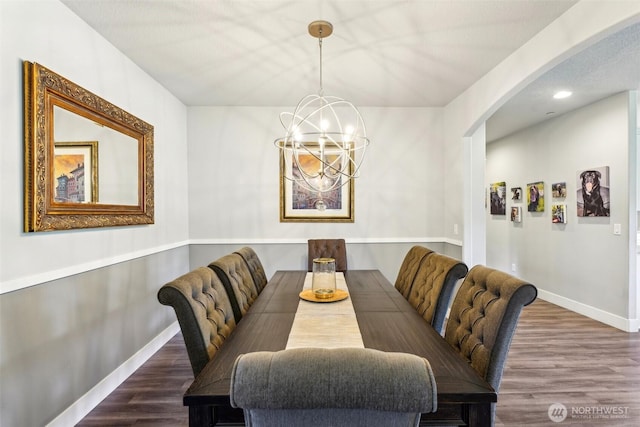 dining space with an inviting chandelier, baseboards, wood finished floors, and arched walkways
