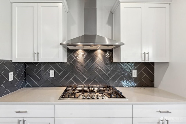 kitchen featuring stainless steel gas stovetop, tasteful backsplash, wall chimney range hood, and white cabinets