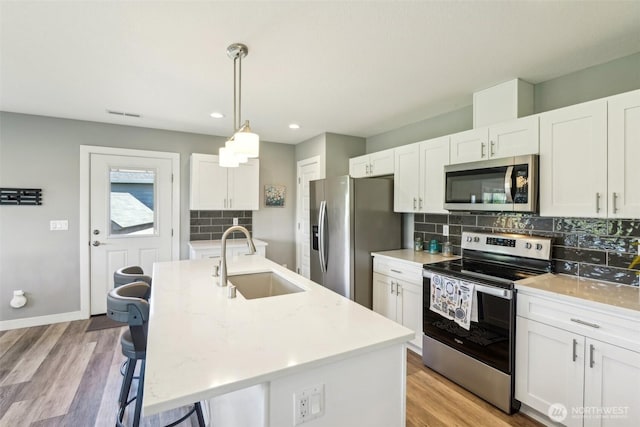 kitchen featuring white cabinets, backsplash, a sink, appliances with stainless steel finishes, and a breakfast bar area