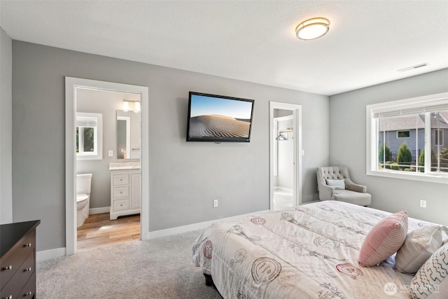 bedroom with light colored carpet, ensuite bath, visible vents, and baseboards