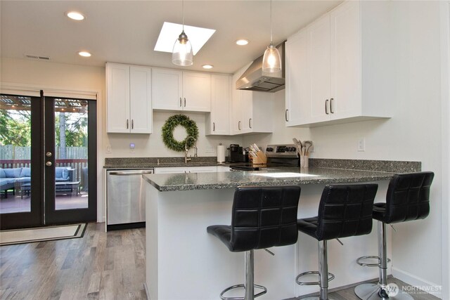 21221 SE 271st Pl, Maple Valley, WA 98038 - kitchen featuring a peninsula, white cabinetry, wall chimney exhaust hood, stainless steel appliances, and wood finished floors