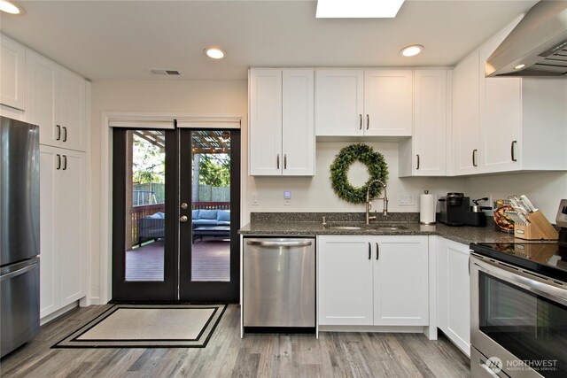 21221 SE 271st Pl, Maple Valley, WA 98038 - kitchen featuring wall chimney range hood, light wood-style flooring, white cabinetry, appliances with stainless steel finishes, and a sink