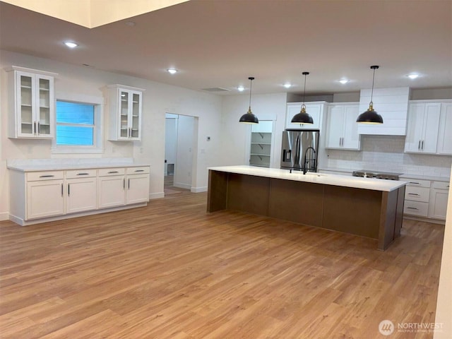 kitchen featuring stainless steel appliances, light wood finished floors, white cabinetry, and backsplash