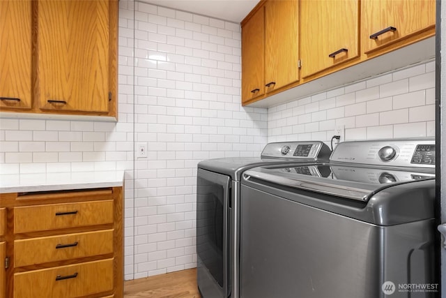 washroom with washer and dryer, light wood-type flooring, tile walls, and cabinet space