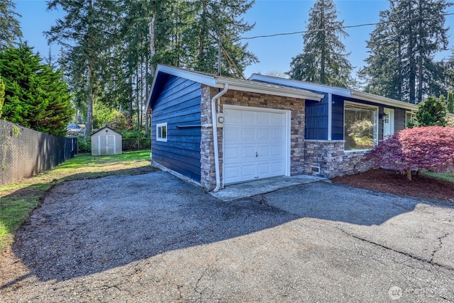garage featuring fence, driveway, and a storage unit