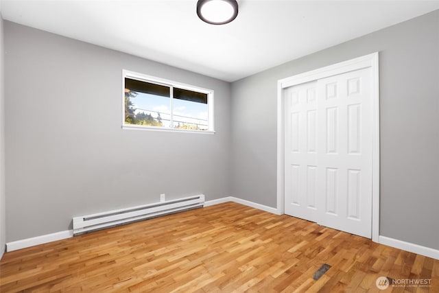 unfurnished bedroom featuring a closet, light wood-style floors, a baseboard radiator, and baseboards
