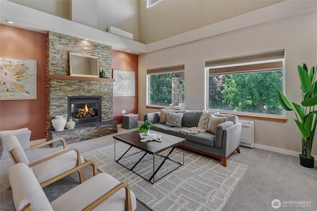 living area featuring baseboards, a towering ceiling, a fireplace, and light carpet