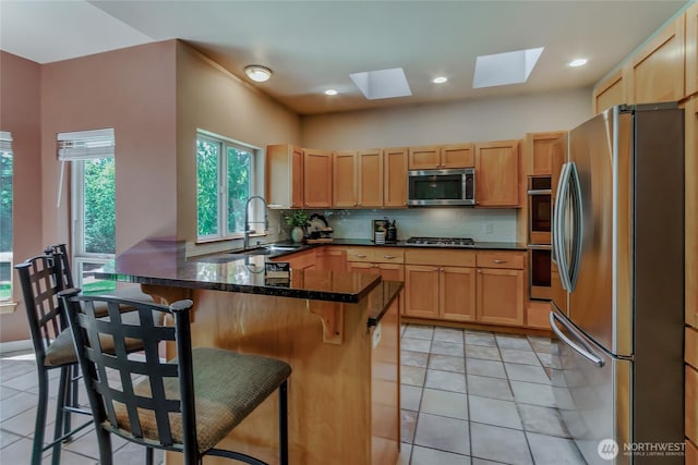kitchen featuring decorative backsplash, a peninsula, a sink, appliances with stainless steel finishes, and a skylight