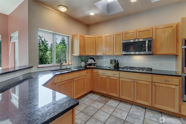kitchen with a sink, a skylight, decorative backsplash, and appliances with stainless steel finishes