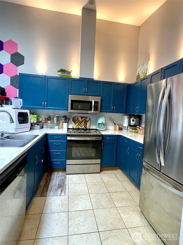 kitchen with blue cabinets, stainless steel appliances, light countertops, and a sink