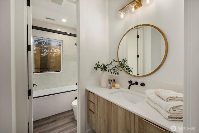 bathroom with vanity, visible vents, toilet, wood finished floors, and enclosed tub / shower combo