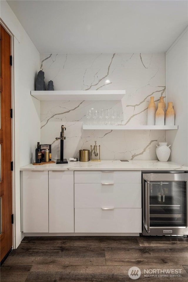 bar with dark wood-style flooring, beverage cooler, backsplash, and a dry bar