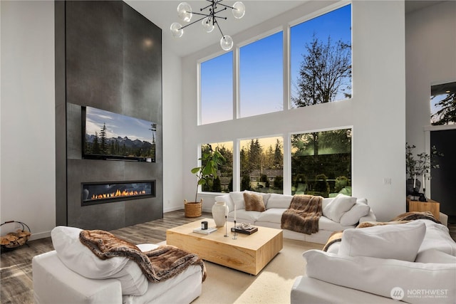living room with a fireplace, a towering ceiling, wood finished floors, baseboards, and a notable chandelier