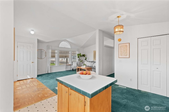 kitchen with tile countertops, vaulted ceiling, carpet floors, a kitchen island, and hanging light fixtures