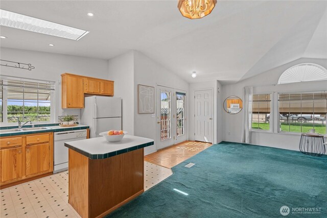 kitchen featuring white appliances, tile countertops, a sink, and lofted ceiling with skylight