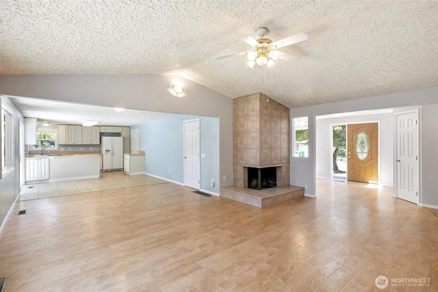 2607 SE 138th Loop, Vancouver, WA 98683 - unfurnished living room featuring light wood-style flooring, a ceiling fan, vaulted ceiling, a fireplace, and a textured ceiling