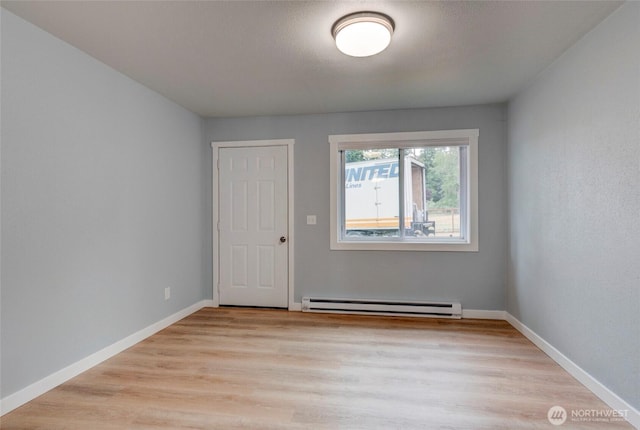 spare room with baseboards, a baseboard heating unit, and light wood-type flooring