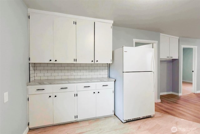 kitchen with freestanding refrigerator, backsplash, baseboards, and white cabinetry