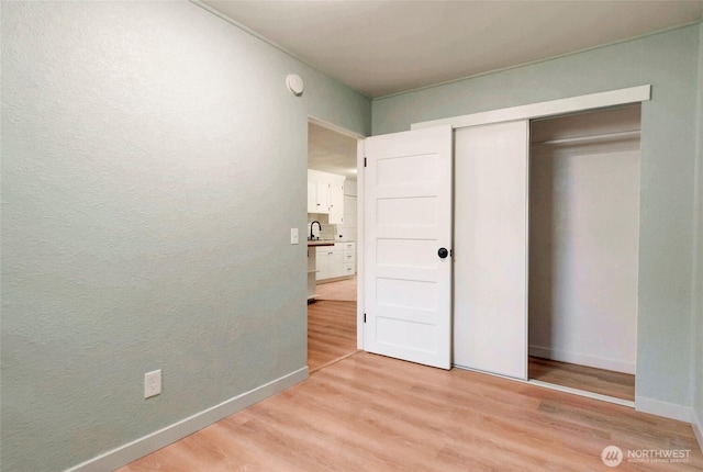 unfurnished bedroom featuring a closet, a textured wall, baseboards, a sink, and light wood finished floors