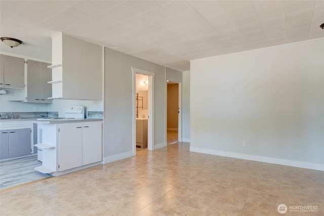 kitchen featuring light countertops, open shelves, baseboards, and range