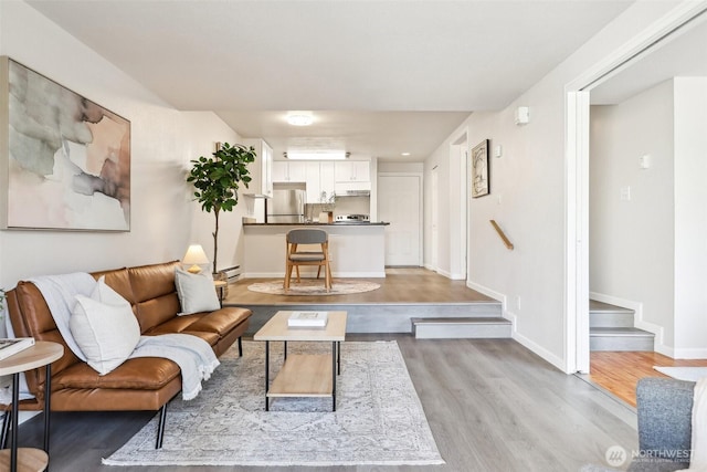 living area featuring a baseboard radiator, baseboards, stairs, and light wood finished floors