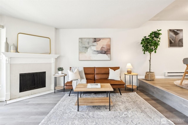 living room featuring a baseboard heating unit, wood finished floors, and a fireplace with flush hearth