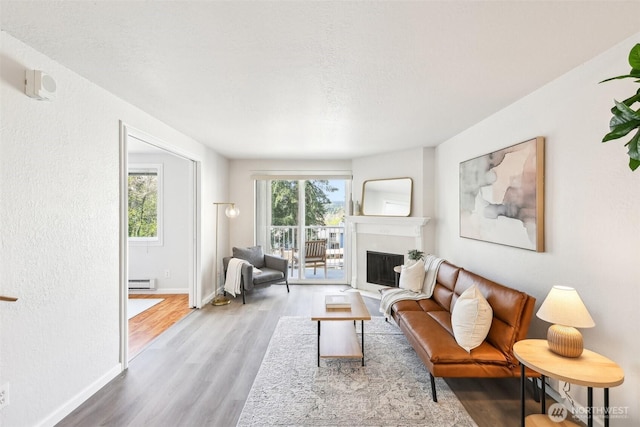 living area with a baseboard heating unit, wood finished floors, a fireplace, and baseboards